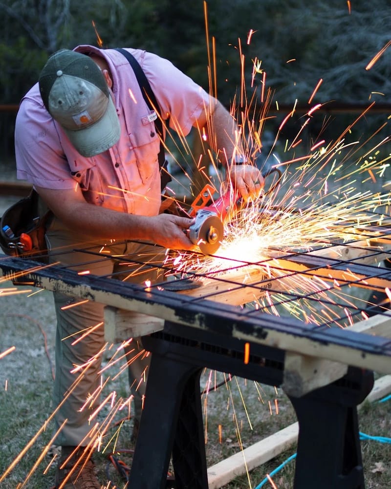 Cutting welded-wire fence panels to size with an angle grinder, sparks flying, on a job in Bastrop County.